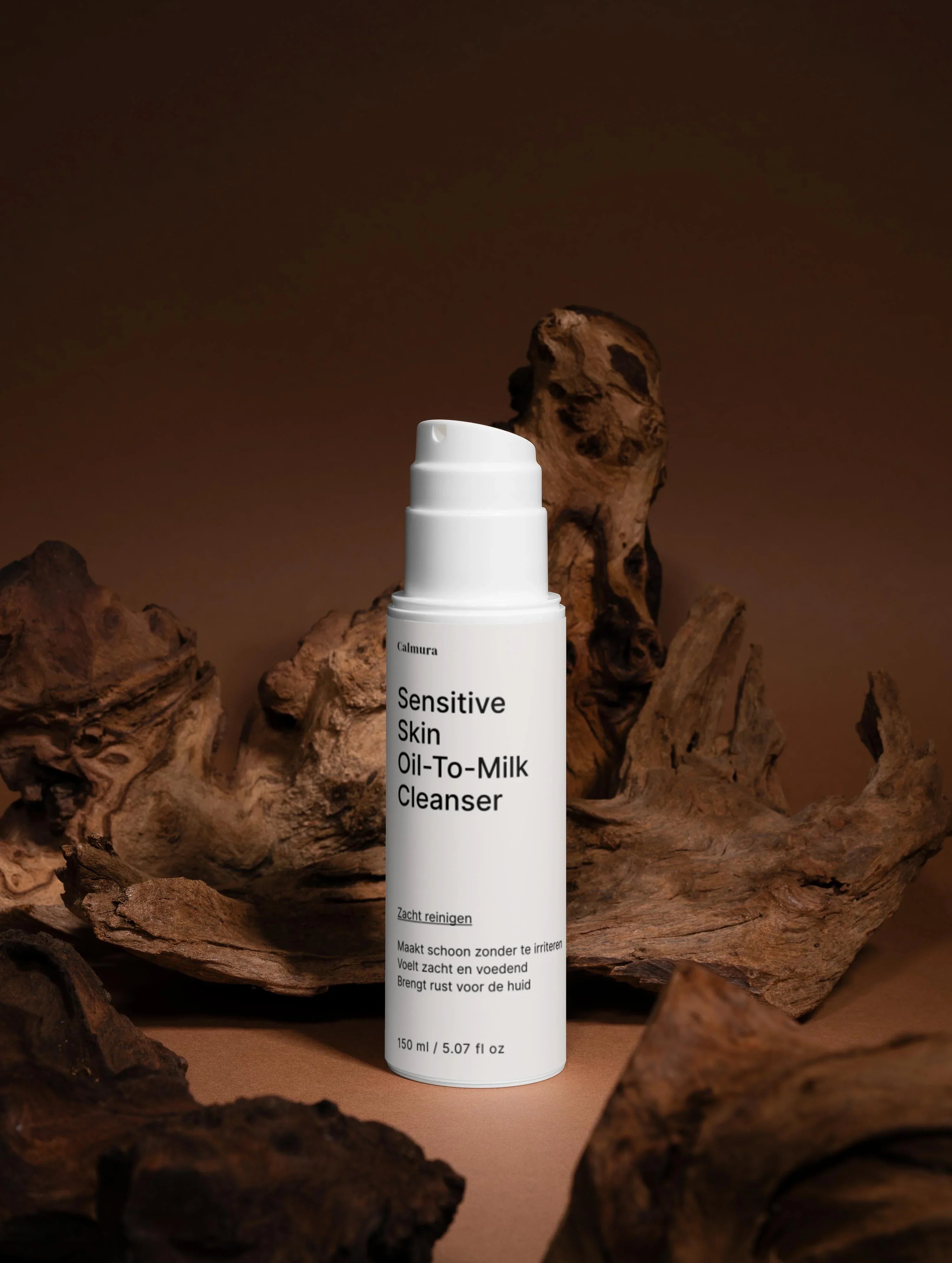 Image of White bottle of Sensitive Skin Oil-To-Milk Cleanser displayed against a dark brown driftwood background.